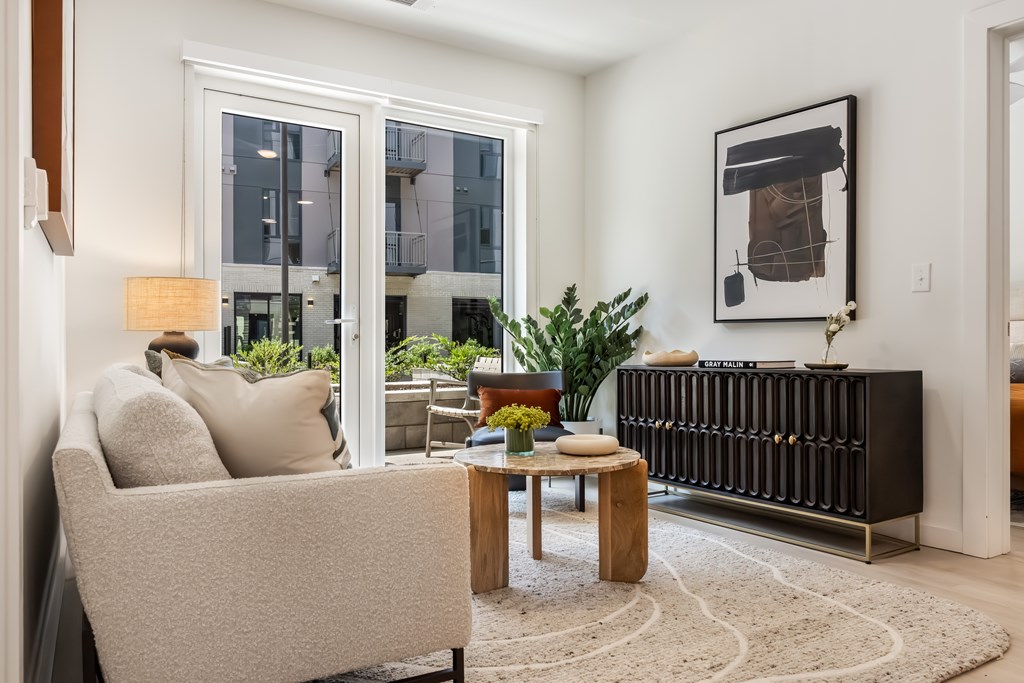 A living room with a beige sofa, a wooden coffee table, and a large window.