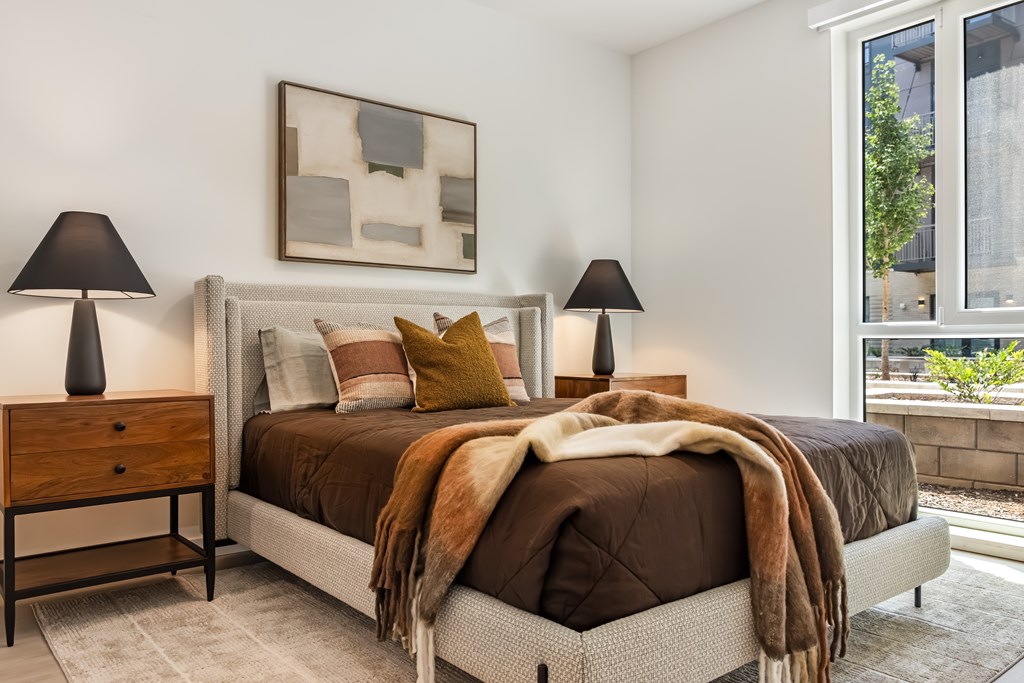 A bedroom with a bed, two lamps, and a painting on the wall.