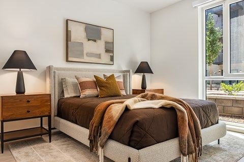 A bedroom with a bed, two lamps, and a painting on the wall.