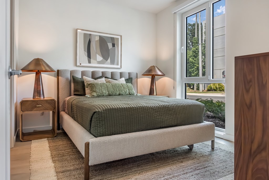 A bedroom with a bed, two lamps, and a painting on the wall.