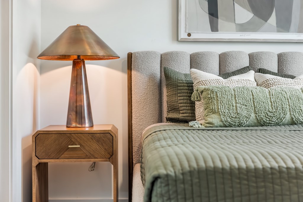 A bed with a green blanket and a lamp on a side table.