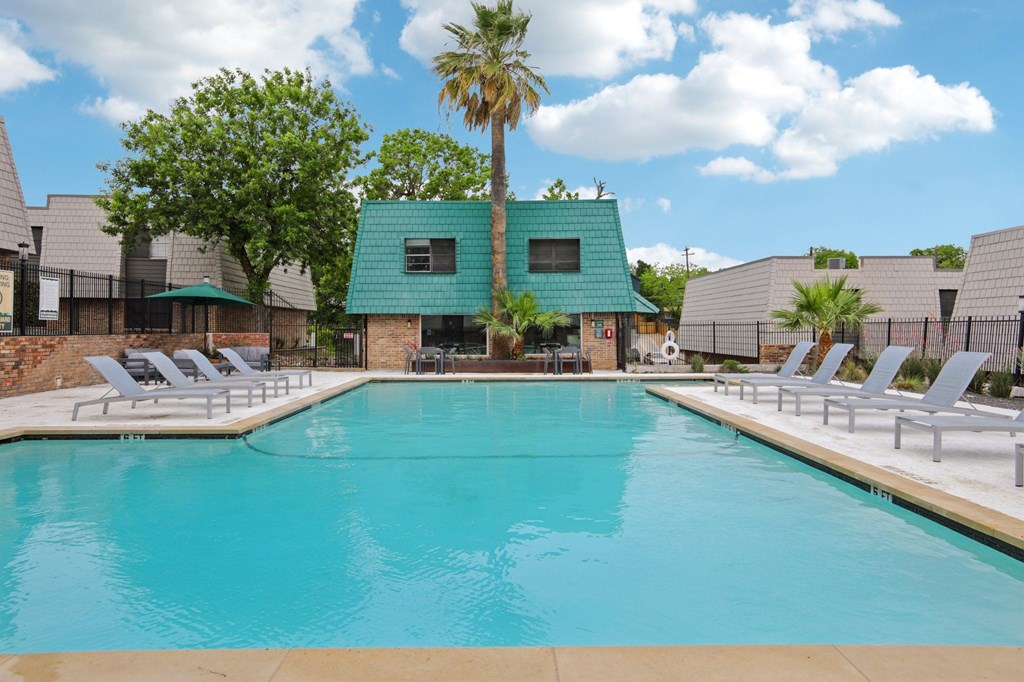 A large swimming pool with lounge chairs and a building with a green roof in the background.