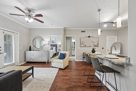 A well-lit, spacious living room with a dining area and a kitchen in the background.