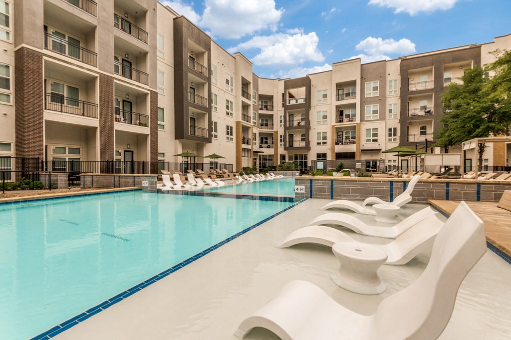 a swimming pool with chaise lounge chairs and umbrellas in front of an apartment building