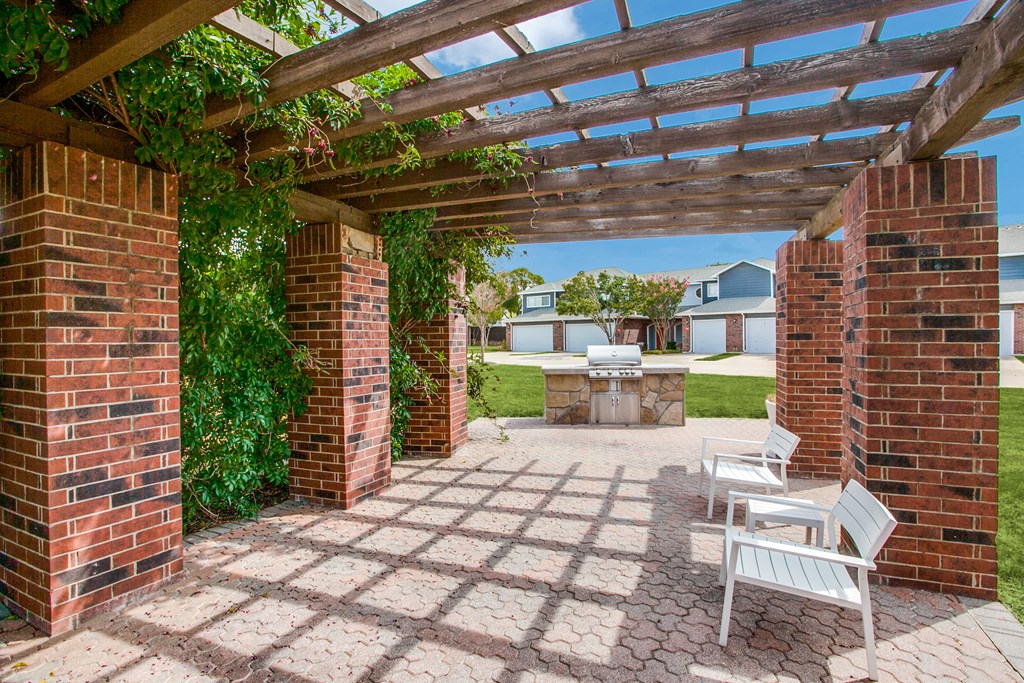 a patio with a pergola and a backyard with a grill