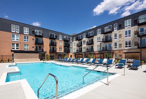 A swimming pool surrounded by lounge chairs in front of apartment buildings.