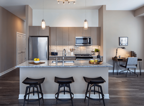 A modern kitchen with a bar area and three stools.