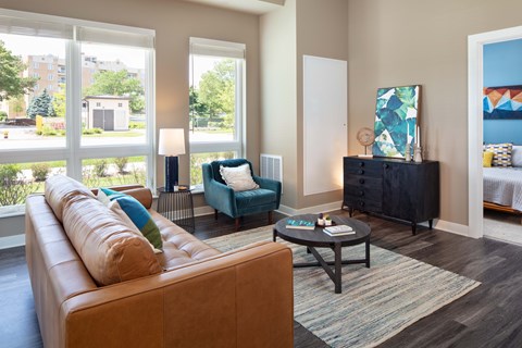 A living room with a brown couch, a blue chair, and a painting on the wall.