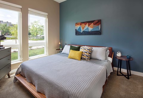 A bedroom with a bed, nightstand, and a painting on the wall.
