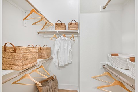 A white closet with clothes and baskets on shelves.