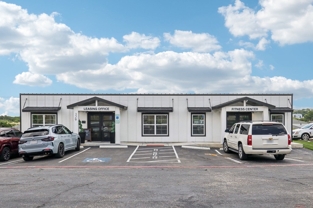 A white building with a sign that says "Fitness Center" is in front of a blue sky with clouds.