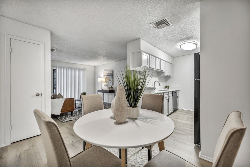 A white dining table with a vase of grass in the middle of it.