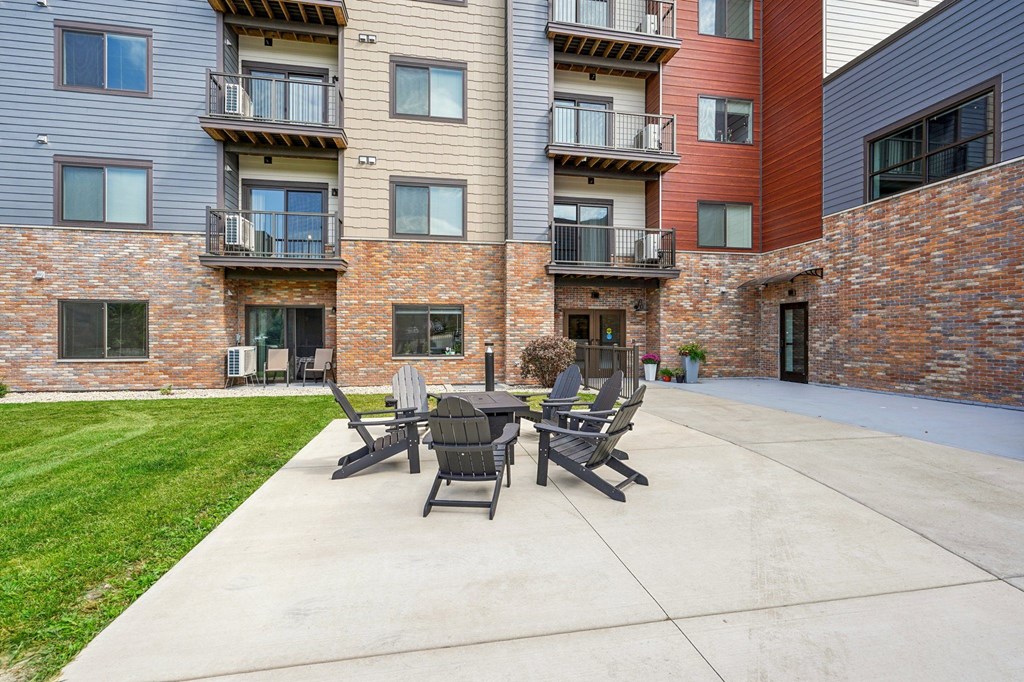 A patio with a table and chairs is in front of a brick wall and apartment buildings.