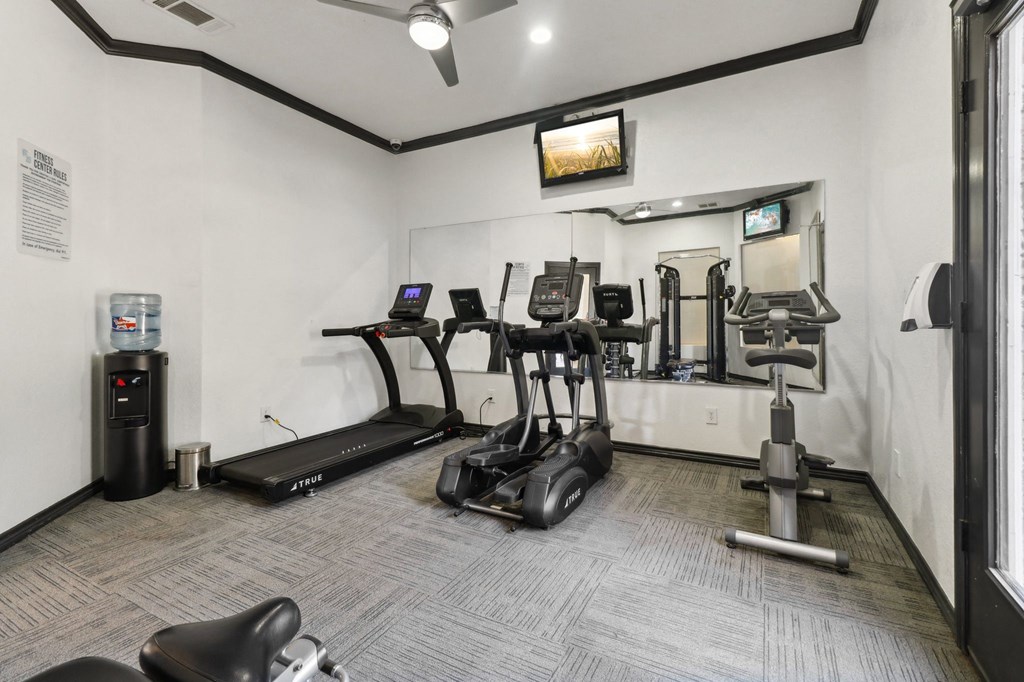A gym with a variety of equipment including treadmills, elliptical machines, and weights.
