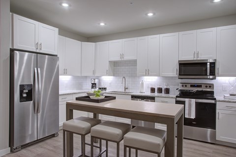 A modern kitchen with a stainless steel refrigerator and a central island with a table and four chairs.