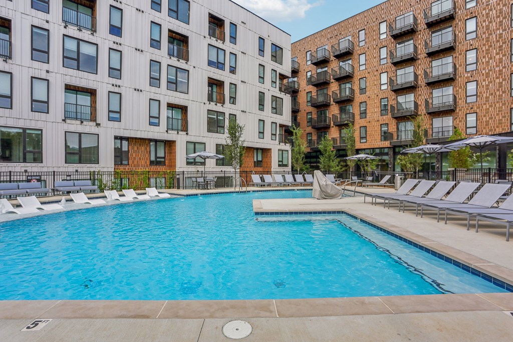 A large outdoor swimming pool surrounded by lounge chairs and buildings.