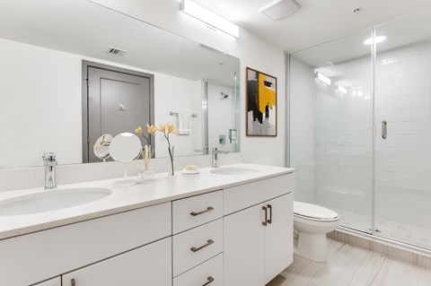 A white bathroom with a sink, mirror, toilet and shower.