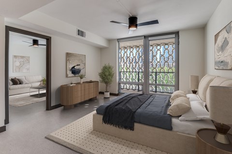 A bedroom with a bed, a couch, a ceiling fan, and a window with a view of trees.