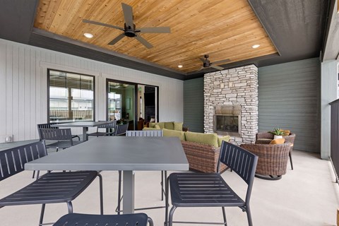 A modern outdoor dining area with a stone fireplace and a ceiling fan.