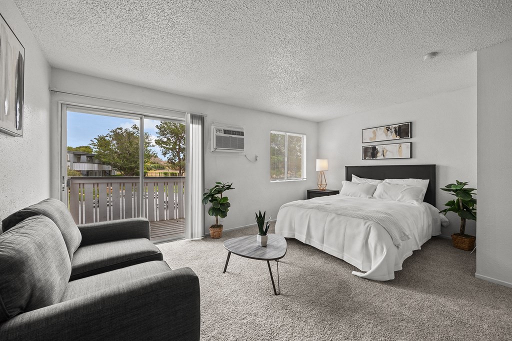 A bedroom with a large bed, grey couch, and a small table.