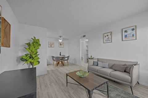 A living room with a grey couch, a wooden coffee table, and a dining table with chairs.