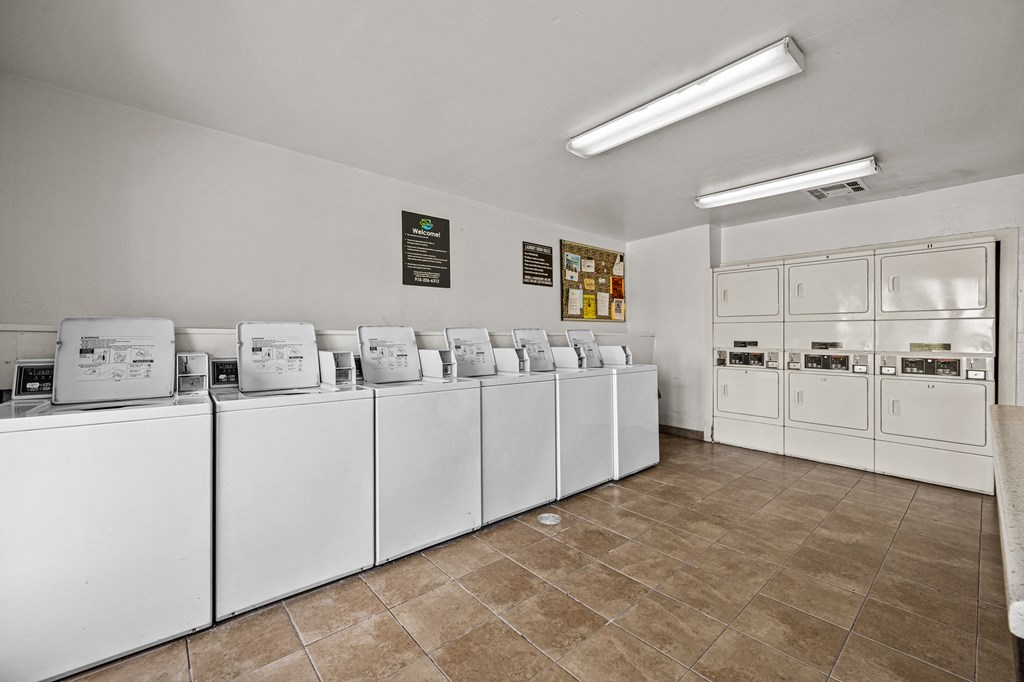 a row of white washers and dryers in a laundry room with tile floor