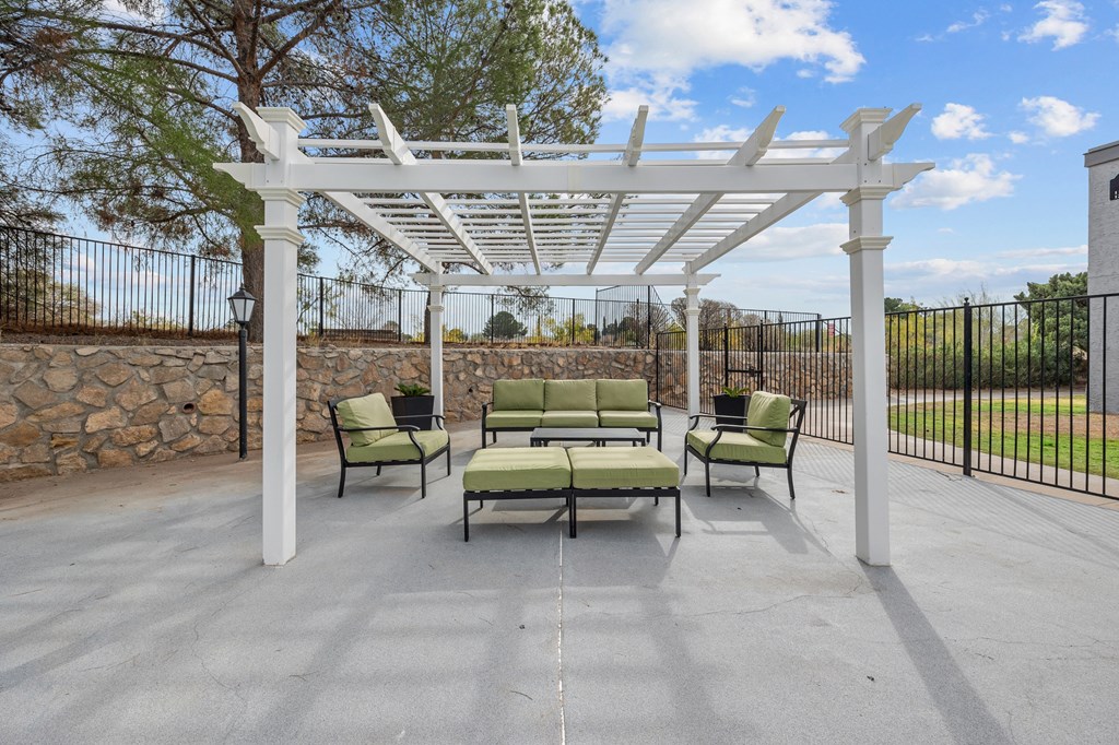 A white pergola with green cushioned chairs is set up on a patio.