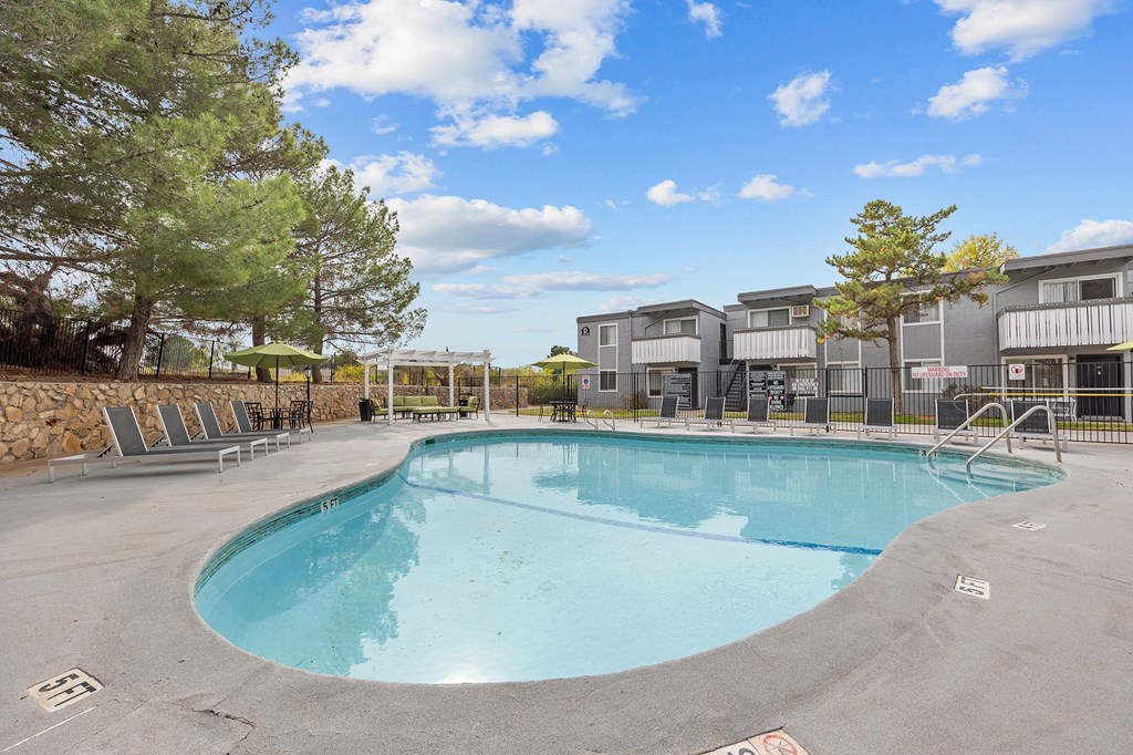 A large outdoor swimming pool surrounded by trees and a building in the background.
