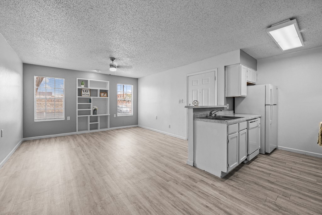 the living room and kitchen of an apartment with white appliances and wood floors
