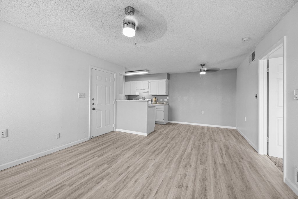 the living room and kitchen of an apartment with white walls and wood flooring