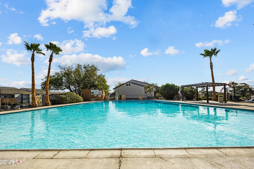 a large swimming pool with palm trees and a building in the background
