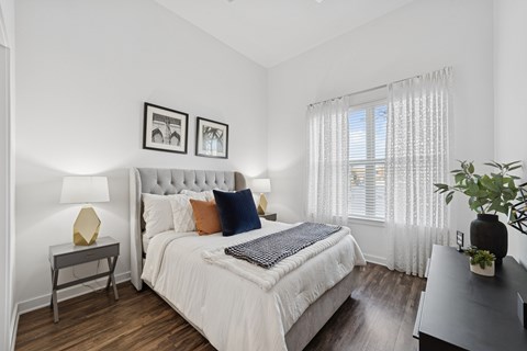 A bedroom with a large bed and a window with white curtains.