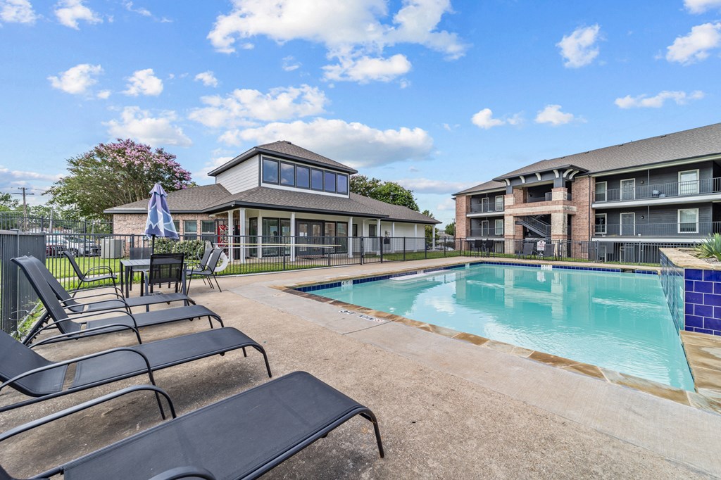 A pool area with lounge chairs and a building in the background.