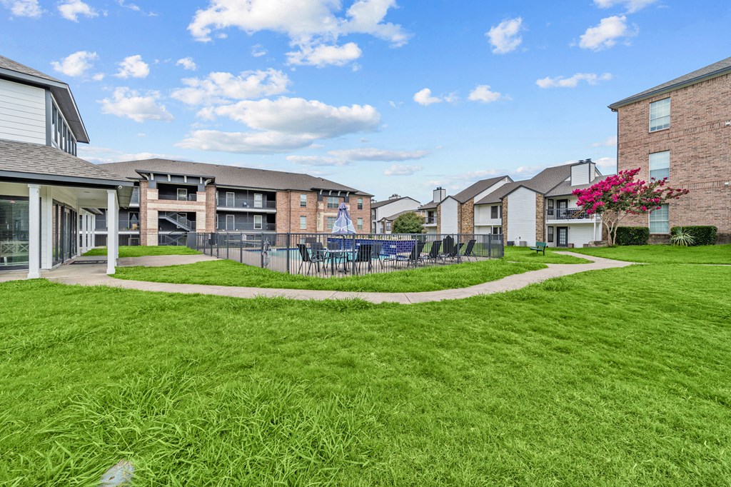 A grassy area in front of apartment buildings with a pink flowering bush.