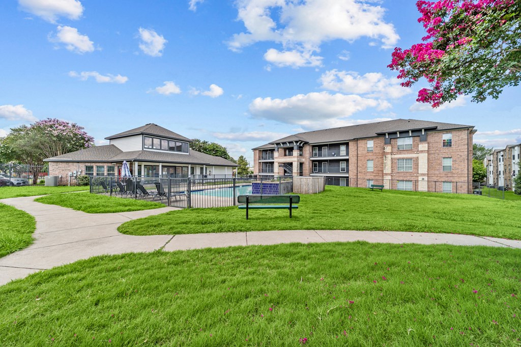 A grassy area with a building and a fence in the background.