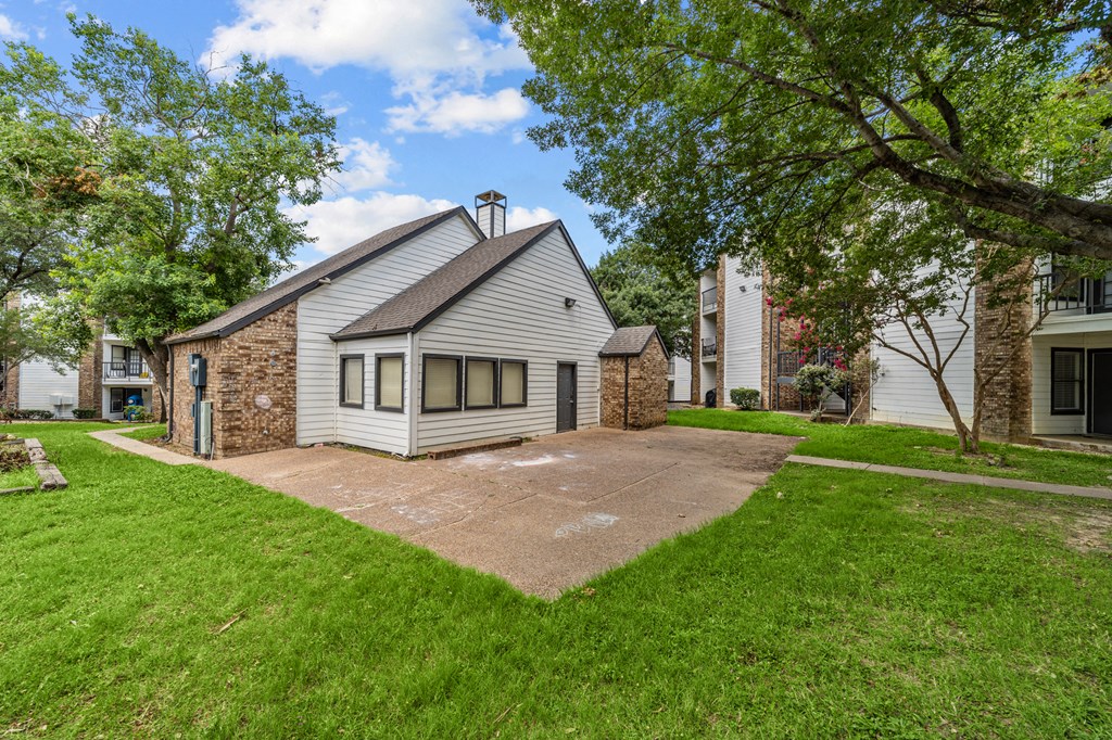 A house with a grey roof and a stone chimney is surrounded by a green lawn.