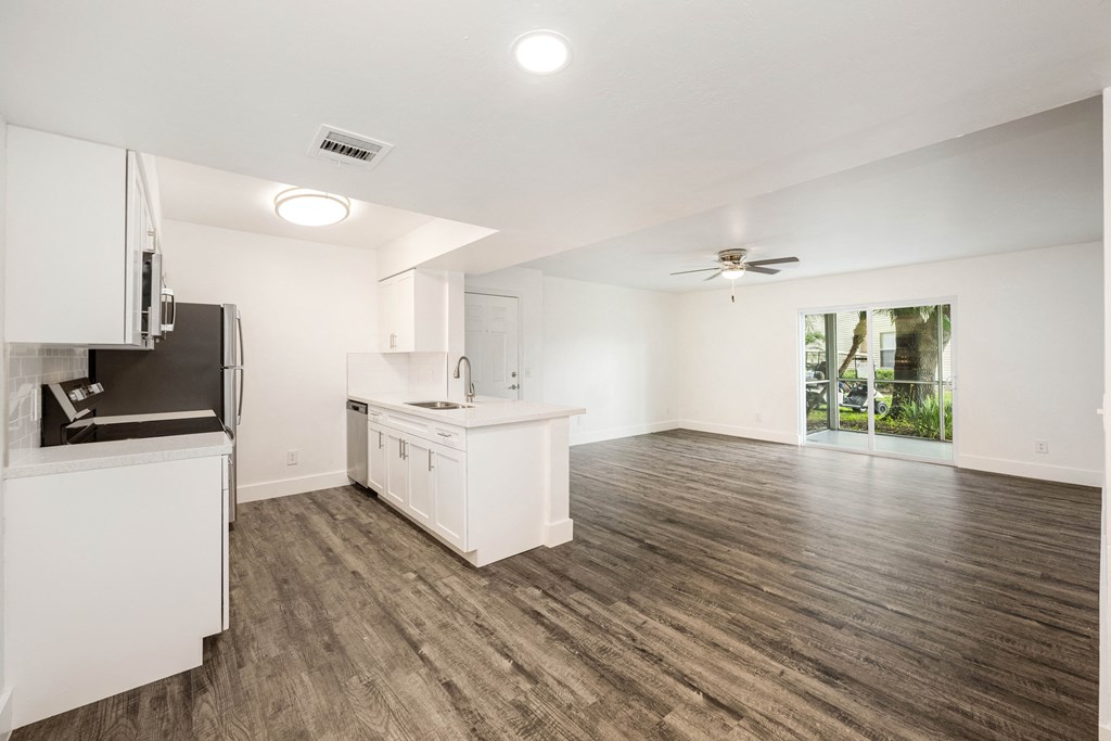 an empty living room with a kitchen and a ceiling fan