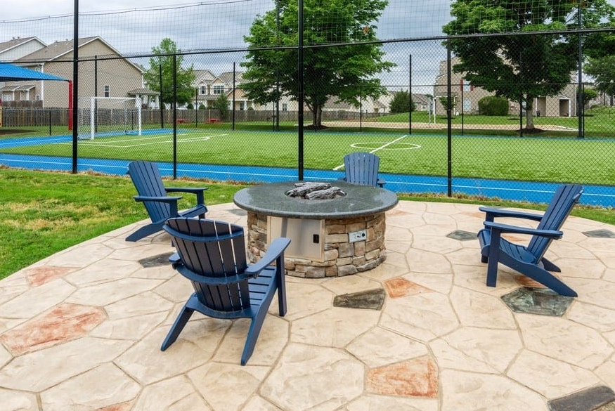 a stone patio with a fire pit and blue adirondack chairs in front of a