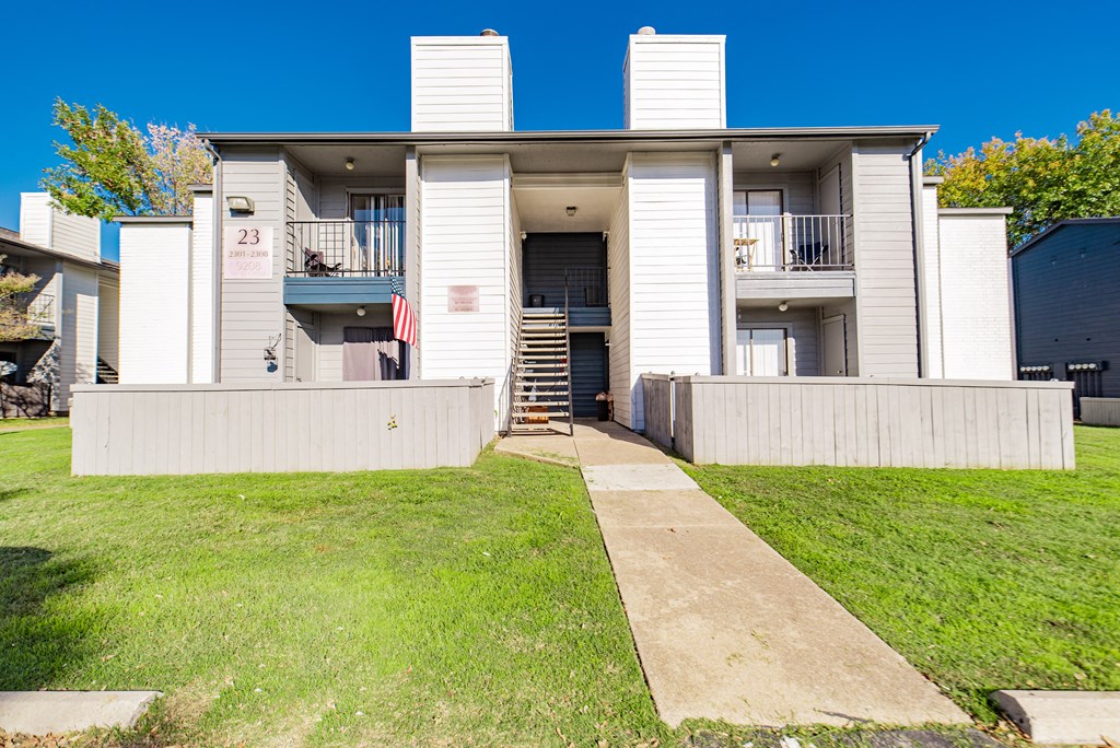 A white two-story house with a balcony and a flag on the front porch.
