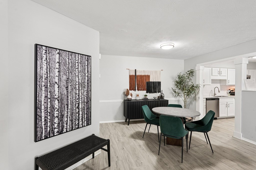 A black and white painting of trees hangs on a white wall above a black bench.