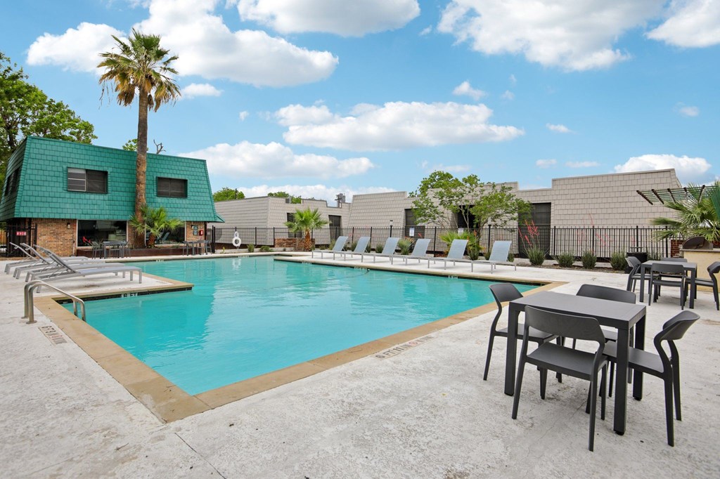 A pool surrounded by chairs and tables with a building in the background.