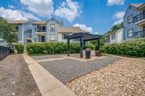 A sunny day at a residential area with apartment buildings and a gravel area with a gazebo.
