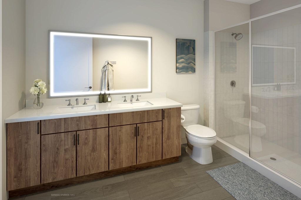A bathroom with a large mirror, a sink with a vanity, a toilet, and a glass shower stall.