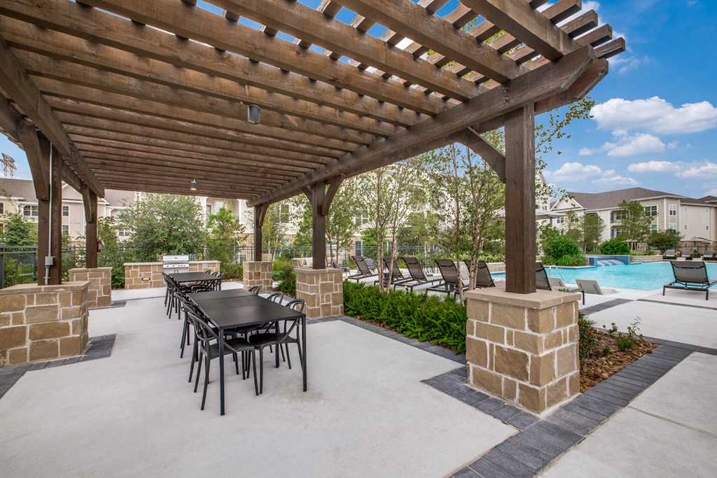 a covered patio with a table and chairs and a pool in the background