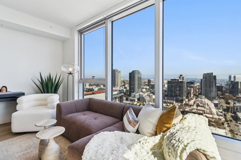 A living room with a brown couch and a large window overlooking a cityscape.