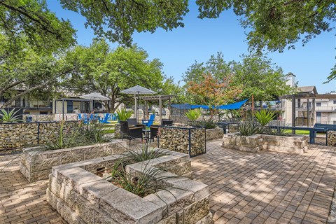 a patio with stone walls and trees and a fountain