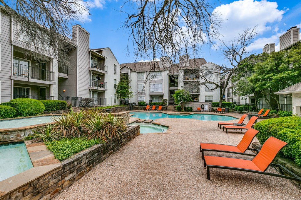 a swimming pool with orange chairs in front of an apartment building