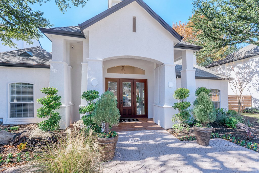 a house with white walls and a front porch with potted trees and shrubs