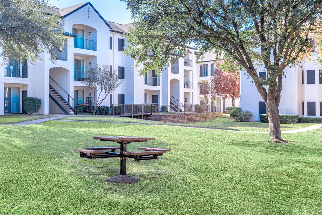 a picnic table sits in the grass in front of an apartment building