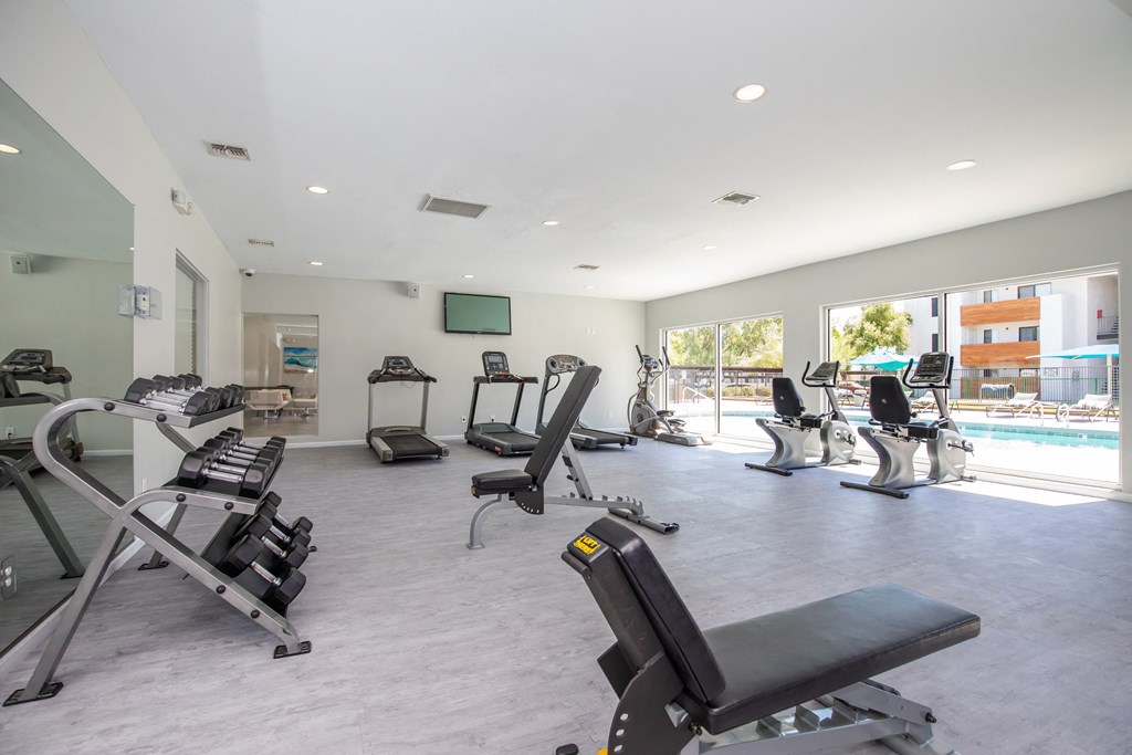 a gym with cardio equipment and a pool in the background